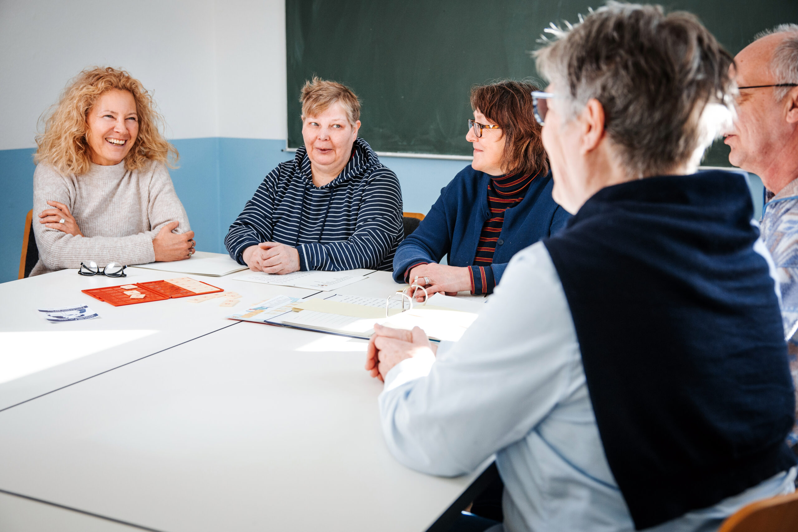 Ehrenamtliche im Lerntandem-Projekt der Volkshochschule Ahrensburg unterstützen Erwachsene mit Lese- und Schreibschwierigkeiten bei einem Treffen im Seminarraum mit Lernmaterialien.